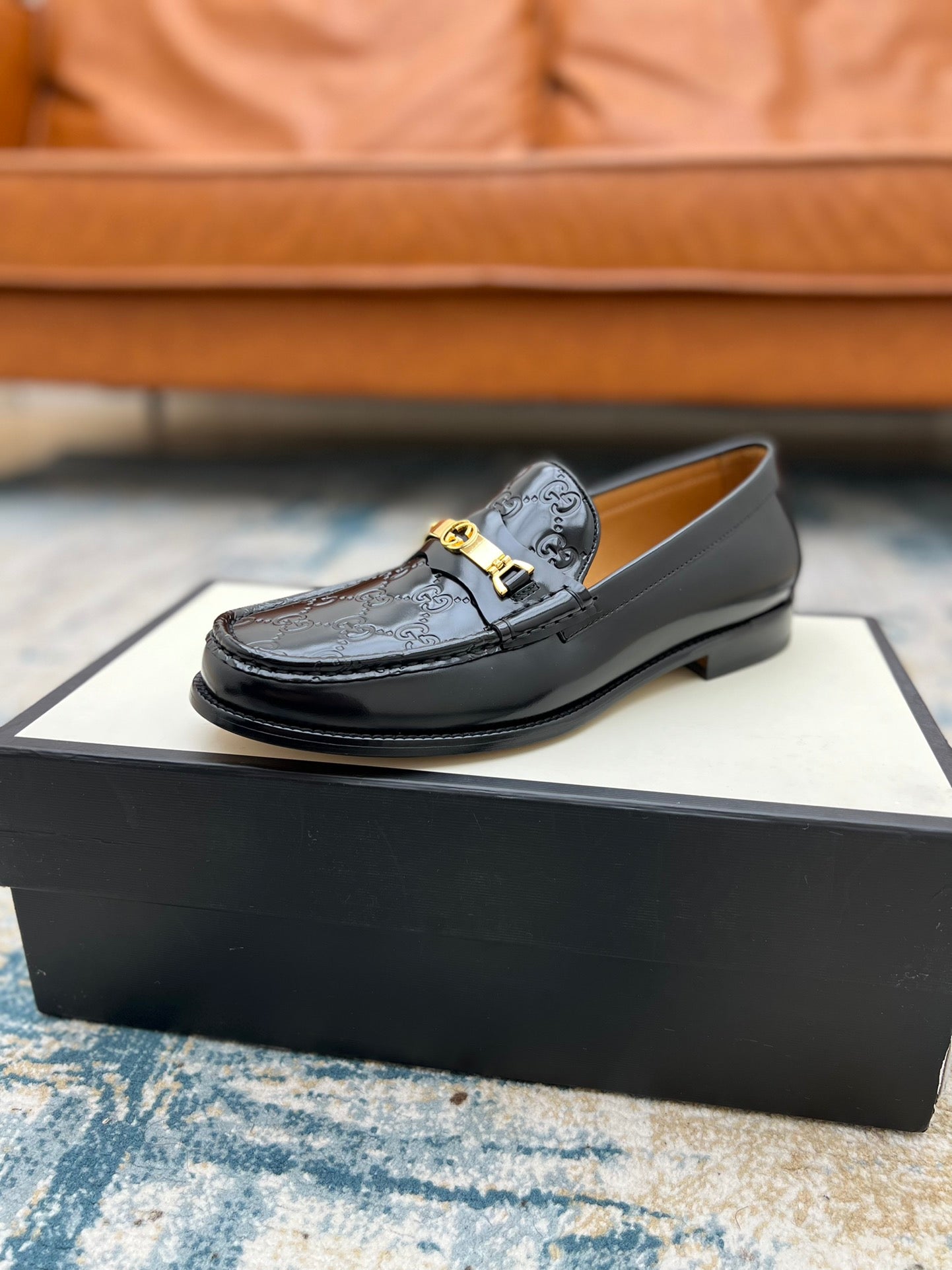 Black Gucci loafer with GG pattern and gold-tone buckle, angled on box