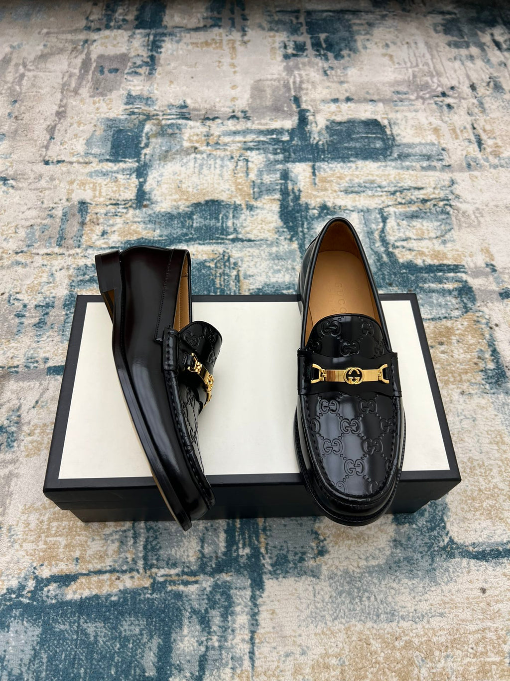 Black Gucci loafers with gold-tone buckle and textured GG print, side view