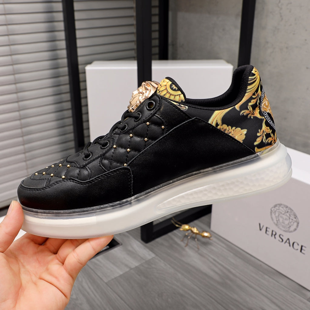 Men's Versace sneakers, black leather with gold patterned strap and white rubber sole.