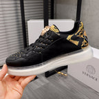 Men's Versace sneakers, black leather with gold patterned strap and white rubber sole.