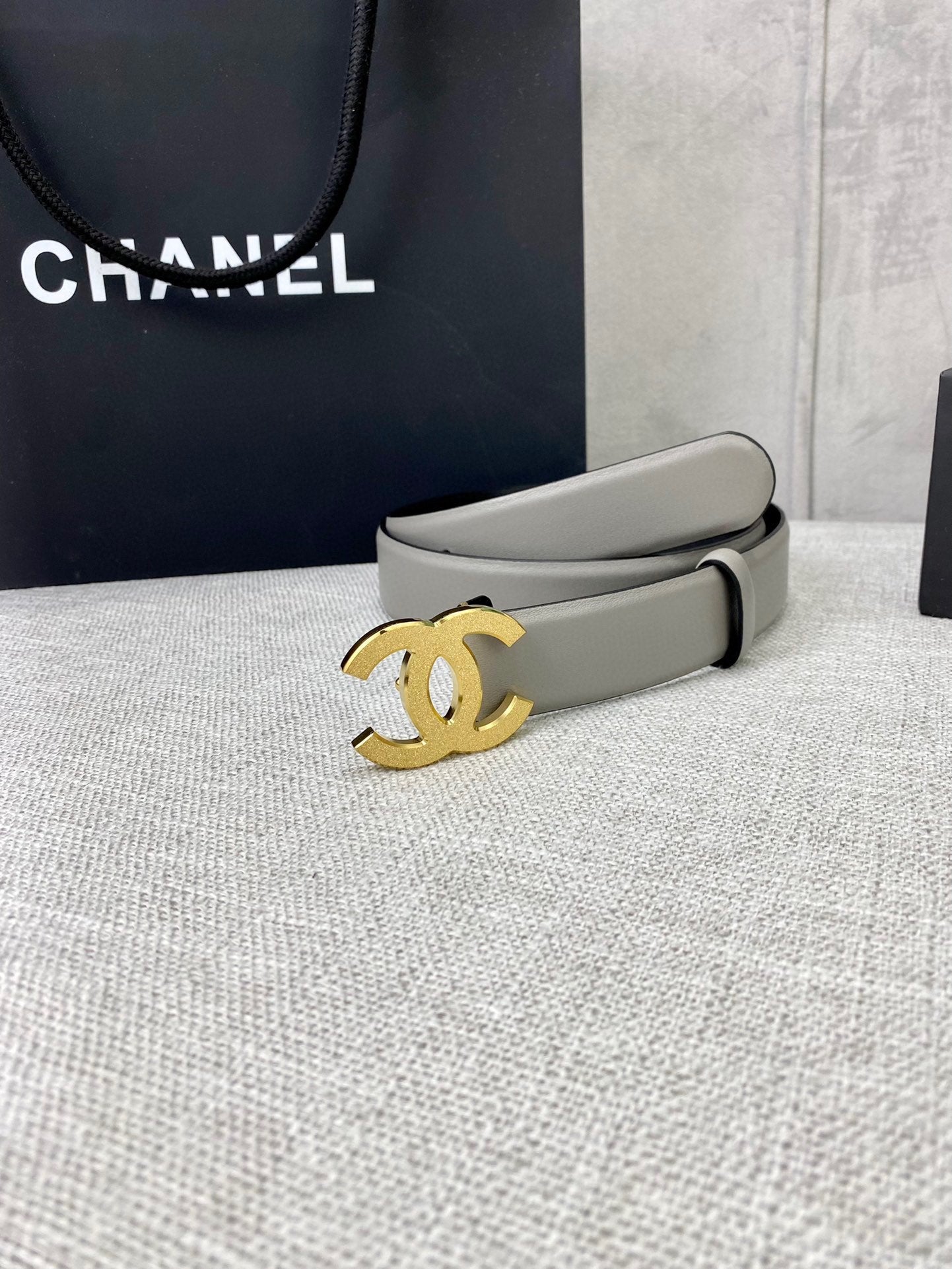 Light gray CC-buckle belt with gold logo buckle, shown near gift box