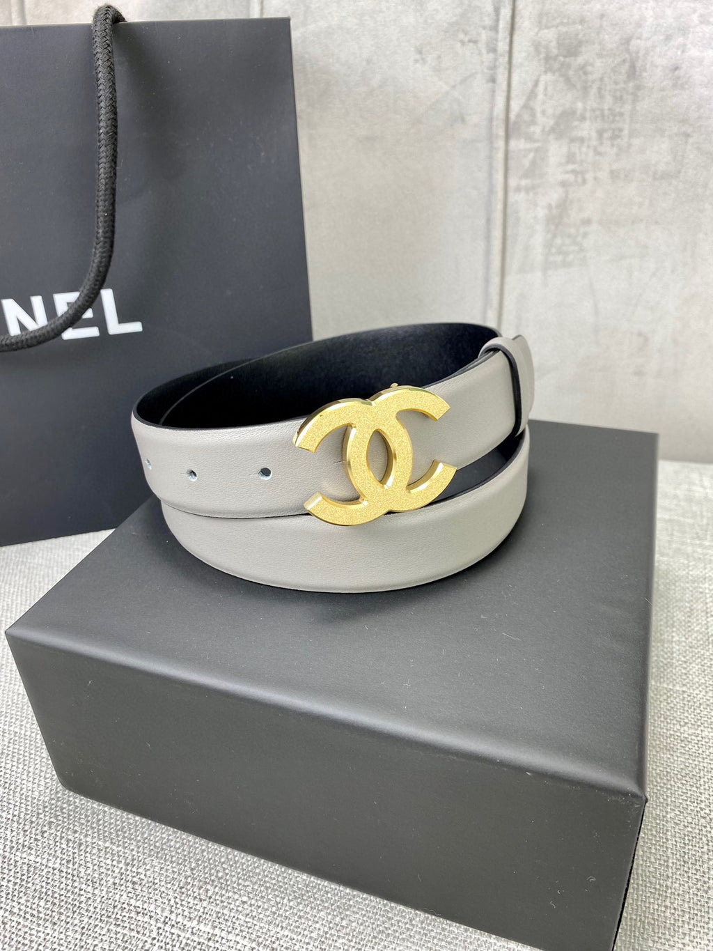 Light gray CC-buckle belt with gold logo buckle on display platform