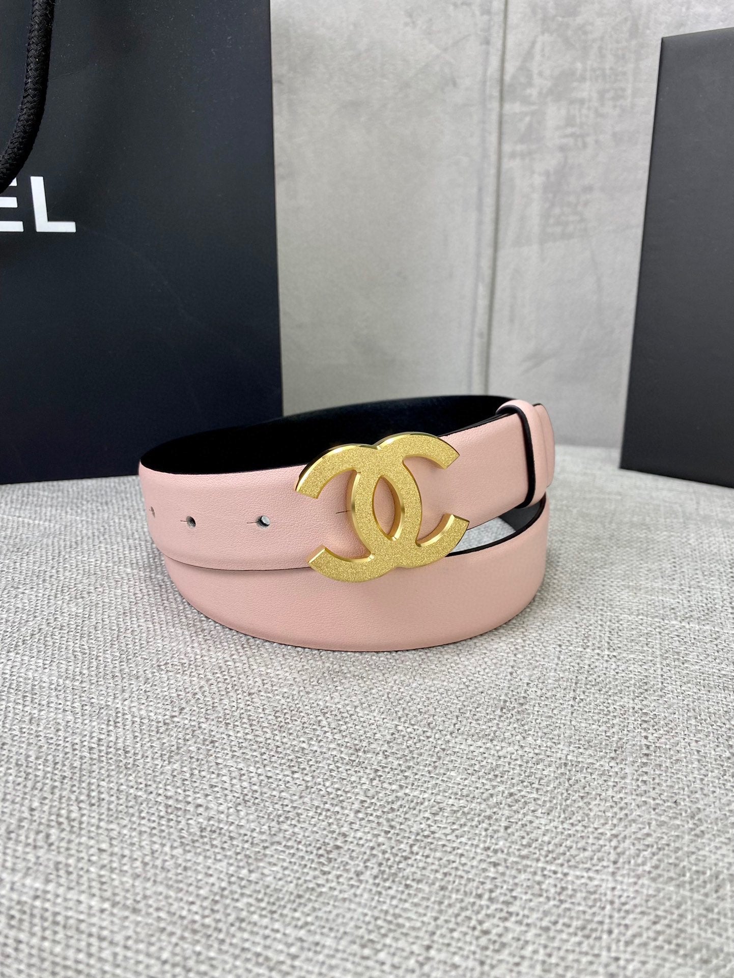 Pale pink leather belt with gold CC emblem centered on the wide strap.