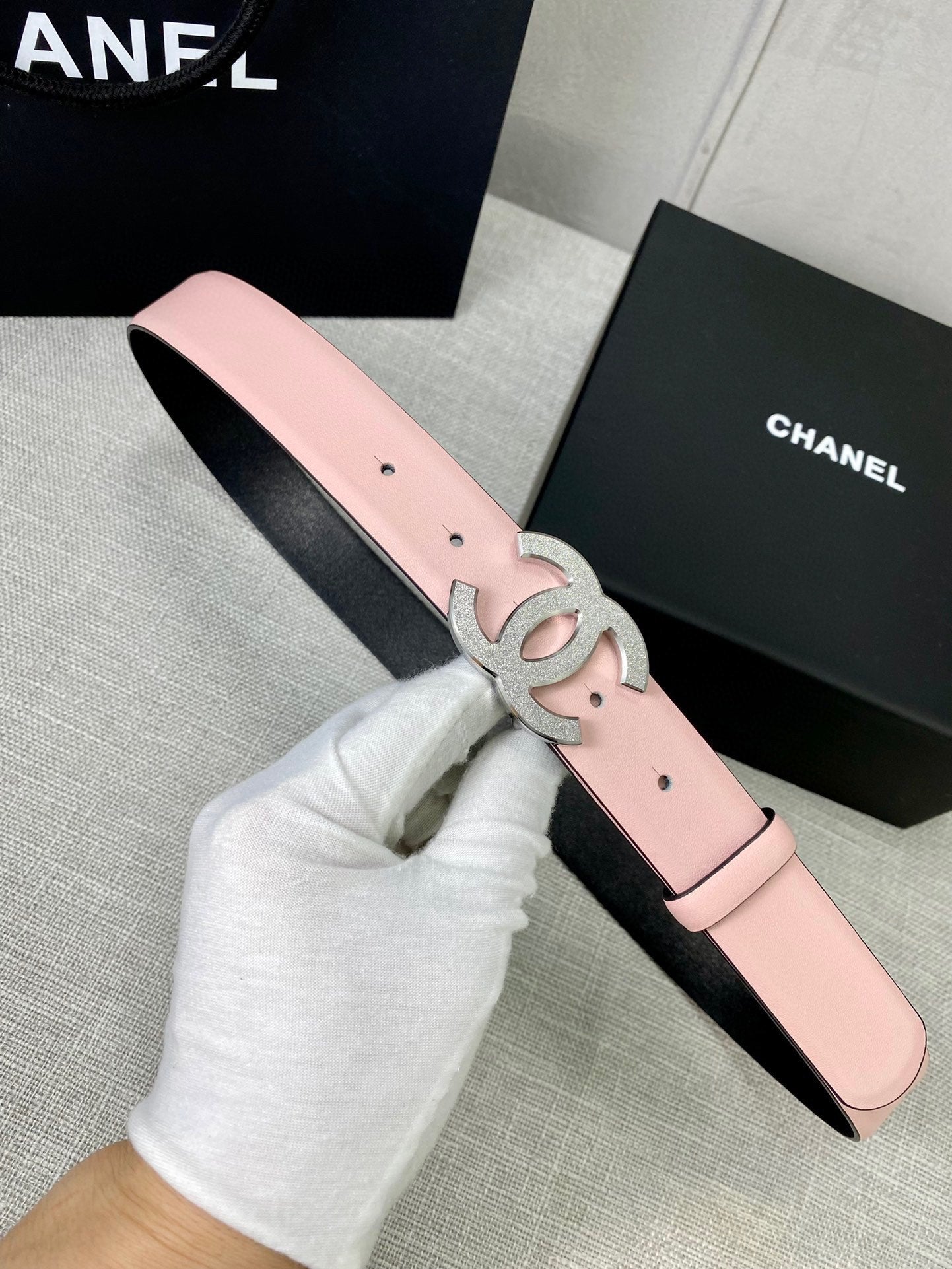 Pale pink leather belt with silver-gray CC buckle emblem and pin-hole strap.