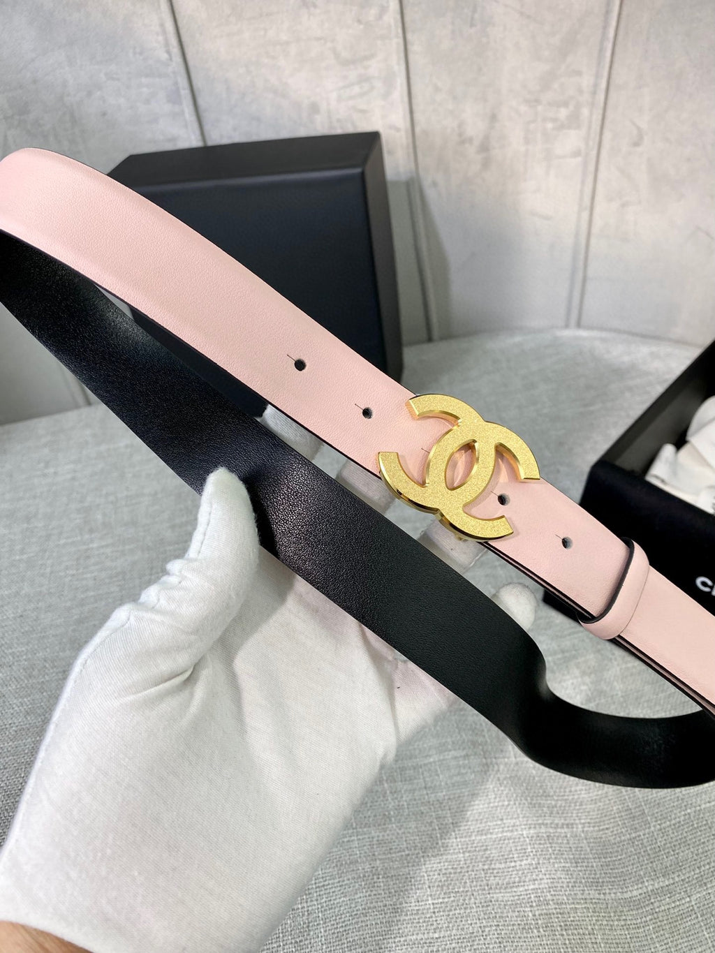 Pale pink belt with gold CC emblem and buckle prong detail, pin-hole strap.