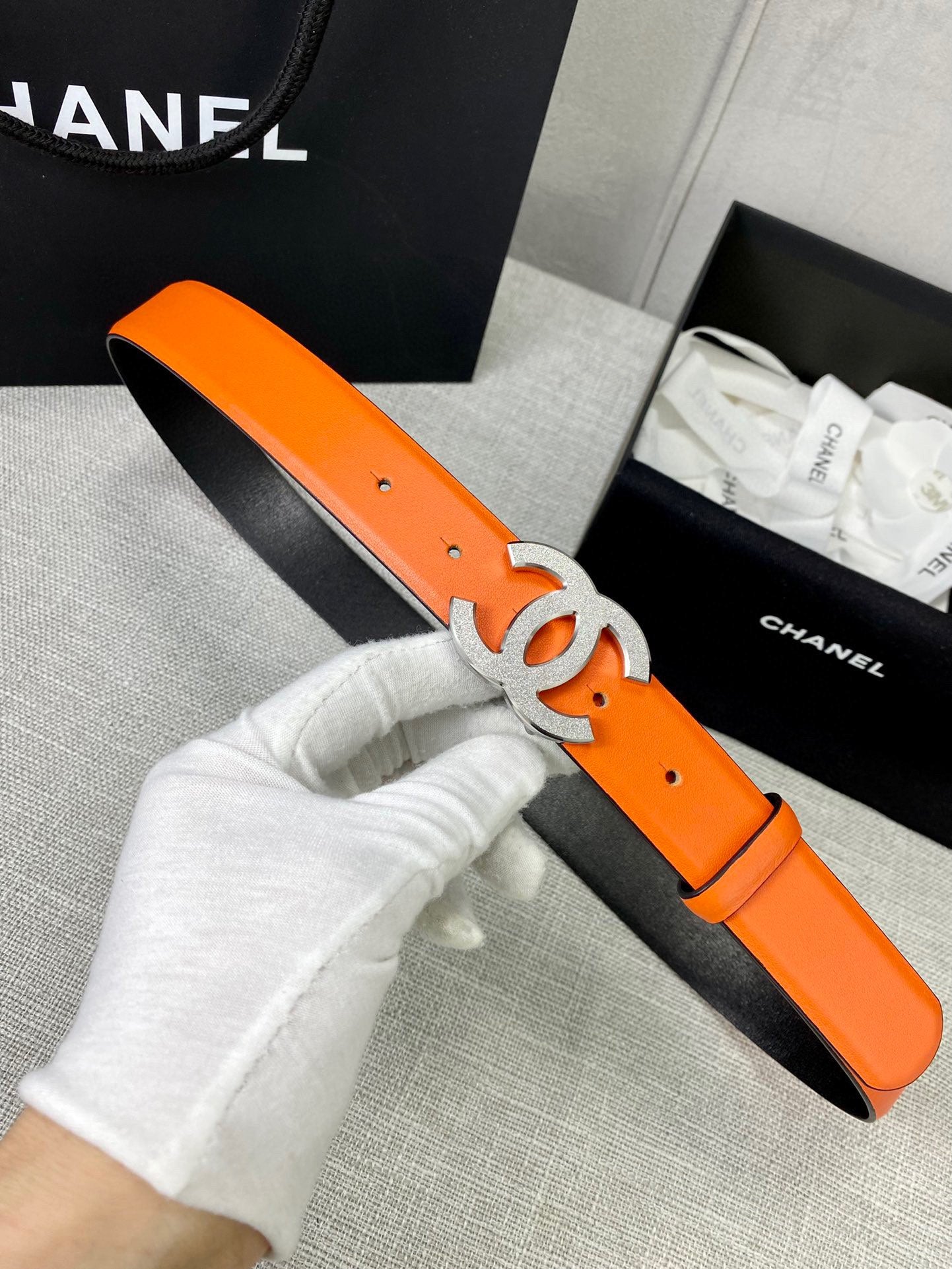 Chanel orange leather belt with gold CC buckle, held by white-gloved hand