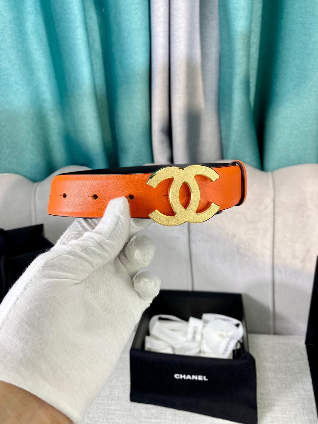 Chanel orange leather belt with gold CC buckle, held in white glove