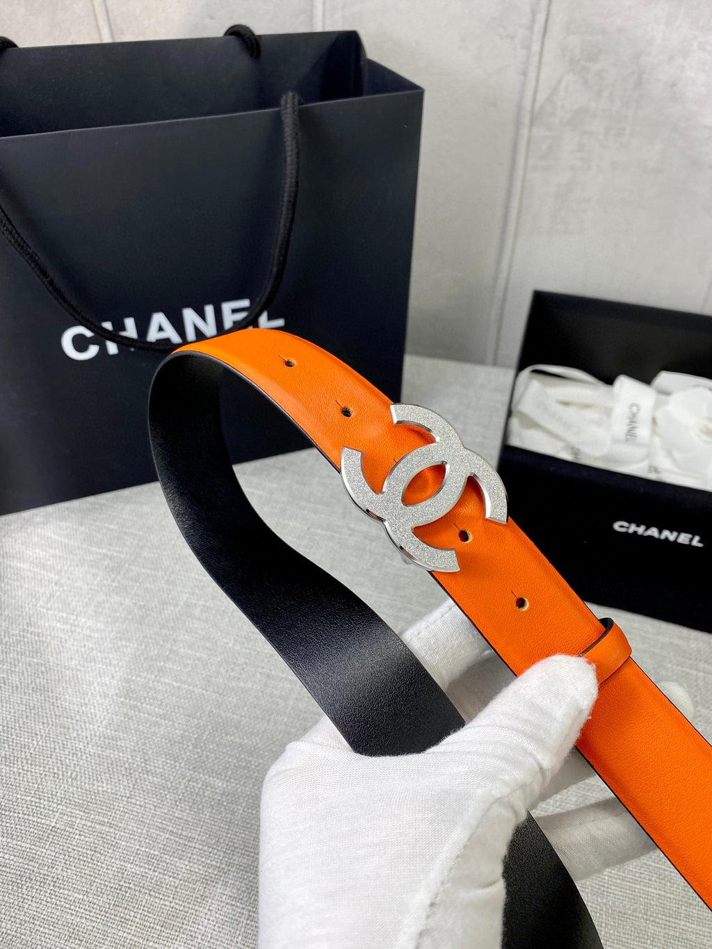 Chanel orange leather belt with silver-toned CC buckle, held by white glove