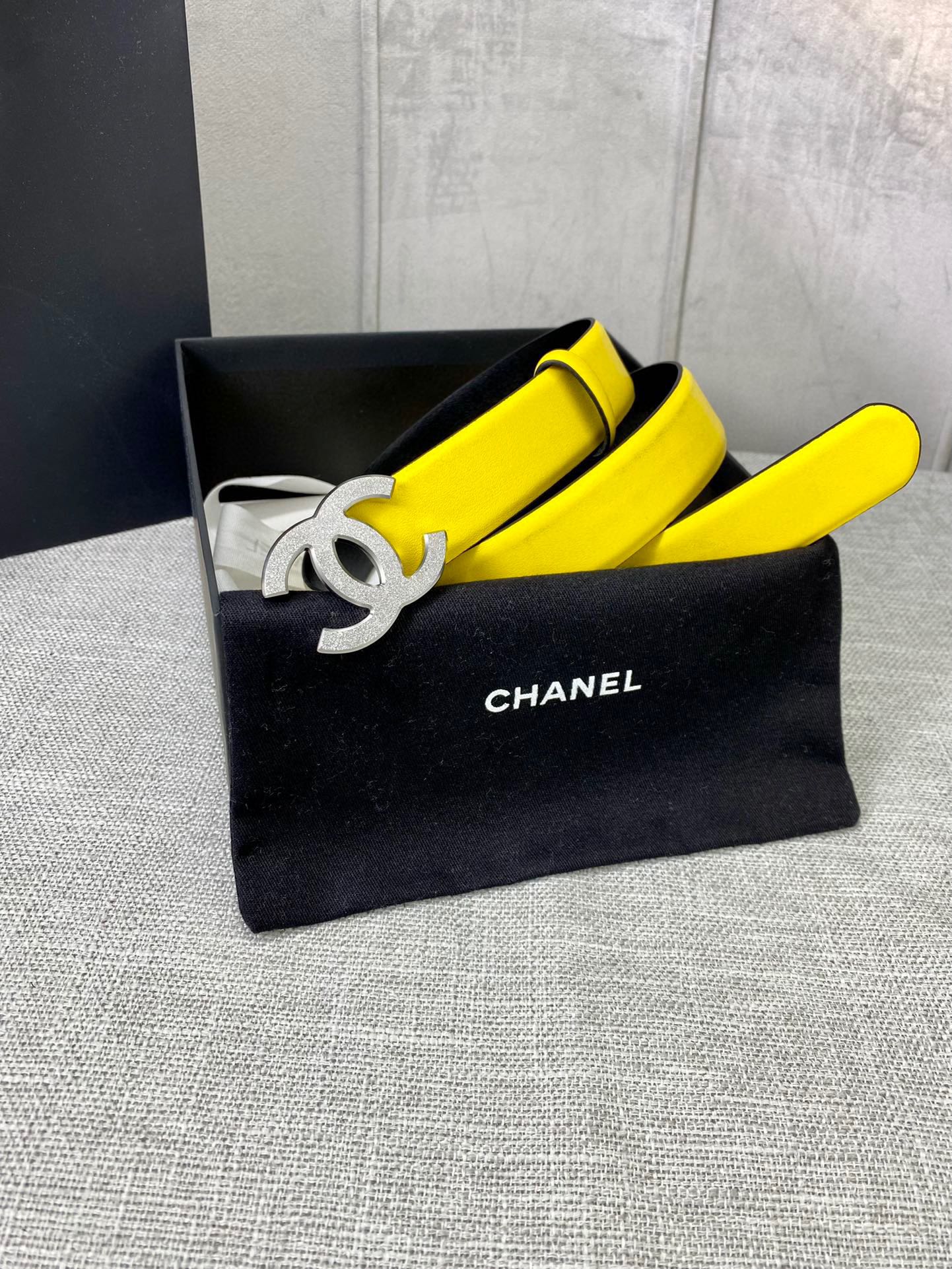 Chanel belt in bright yellow with gold CC logo buckle, resting in black pouch