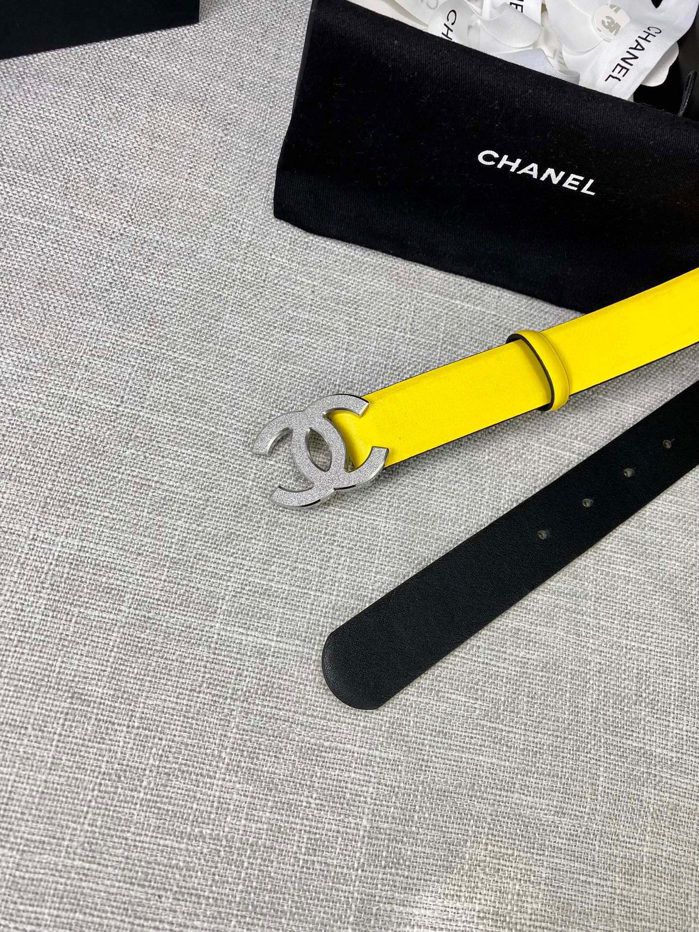 Chanel belt close-up: bright yellow strap with gold CC logo and punched holes