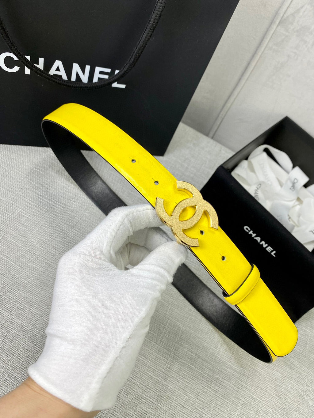 Chanel belt on gloved hand: bright yellow strap with gold CC buckle