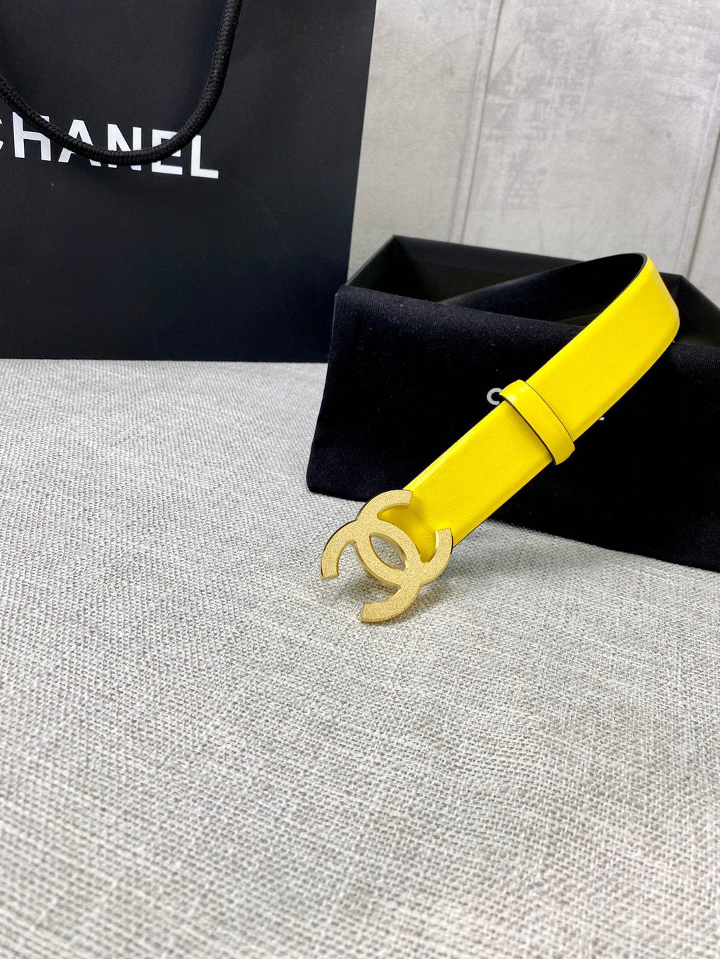 Chanel belt in bright yellow leather with gold CC buckle, beside black gift box