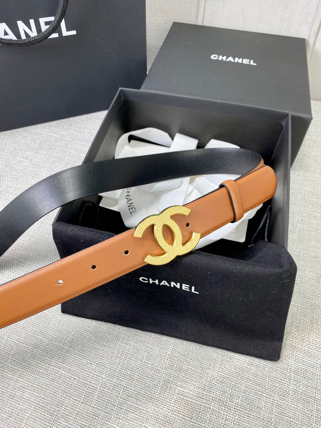 Tan leather belt with gold-tone CC buckle, laid across box tissue.