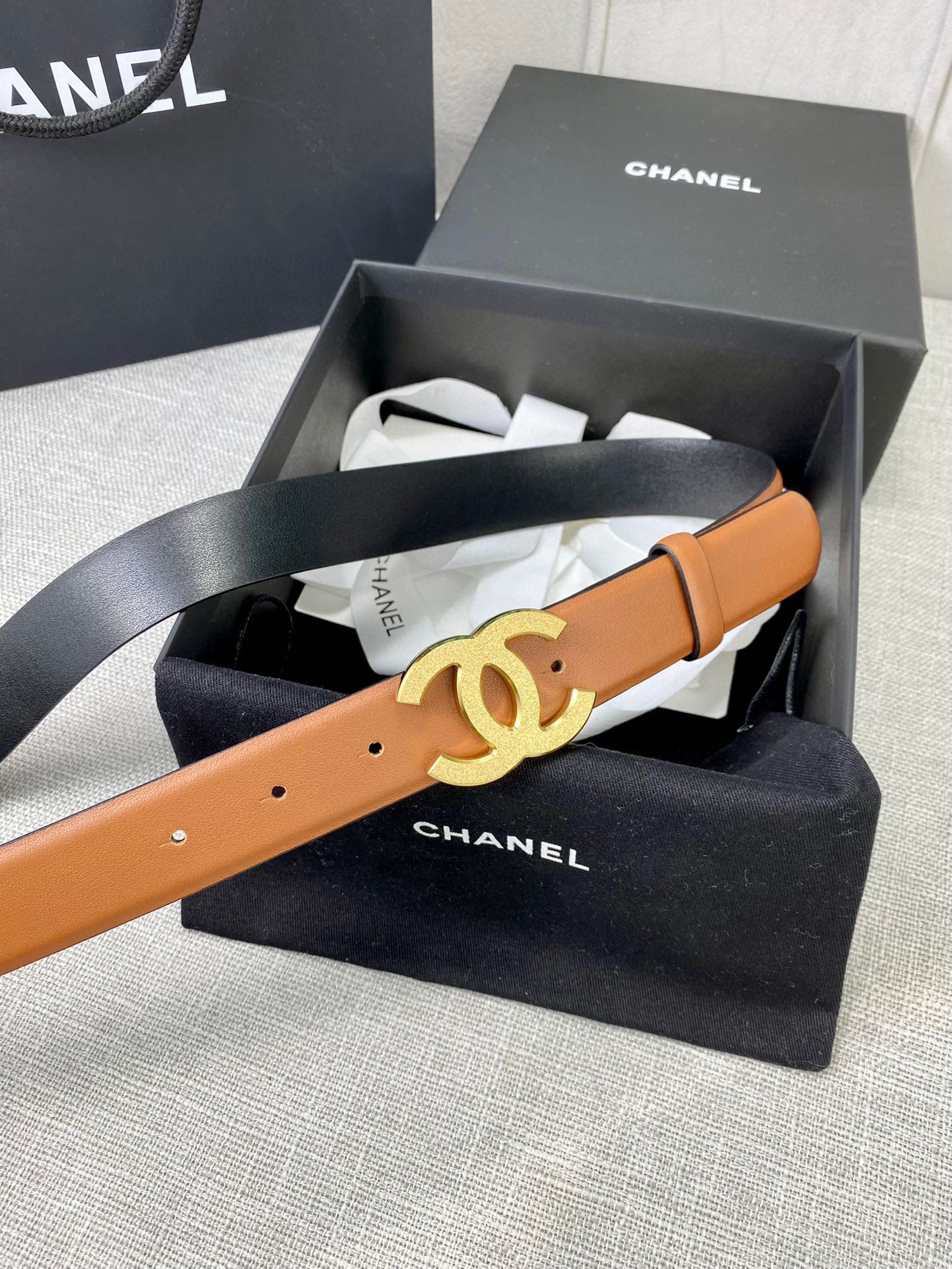 Tan leather belt with gold-tone CC buckle, laid across box tissue.