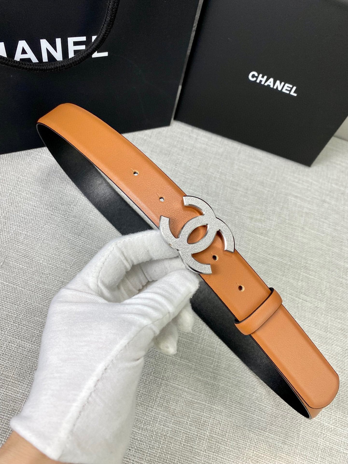 Tan leather belt with gold-tone CC buckle, held in white gloves.