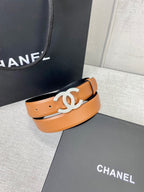 Tan leather belt with gold-tone CC buckle, resting on black box lid.