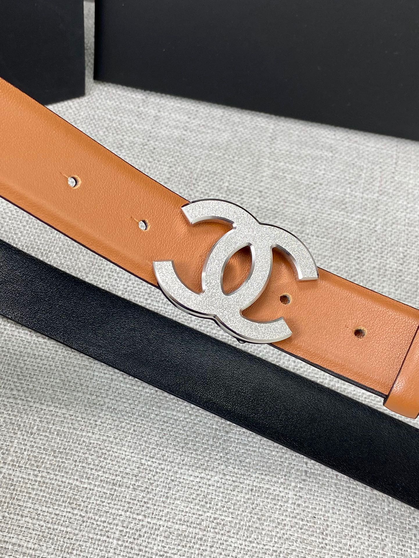 Tan leather belt with gold-tone CC buckle, close-up of buckle and holes.