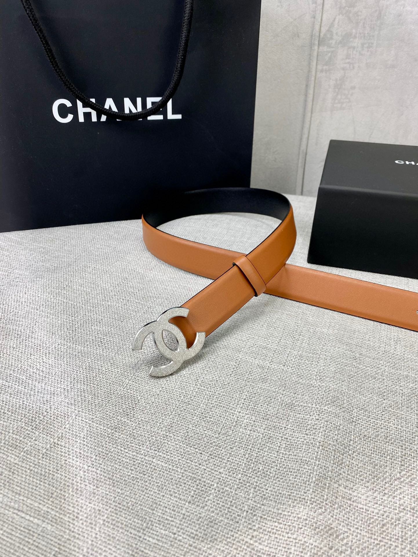 Tan leather belt with gold-tone CC buckle and strap end detail.