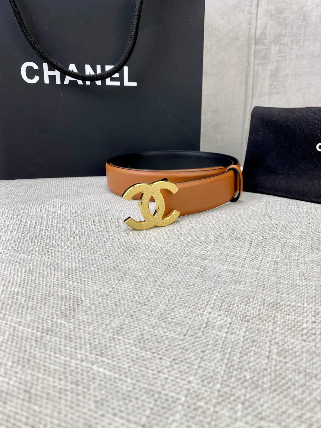 Tan leather belt with gold-tone CC buckle, on tabletop display.