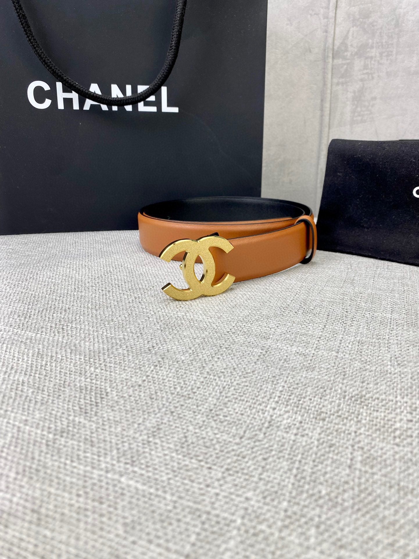 Tan leather belt with gold-tone CC buckle, on tabletop display.