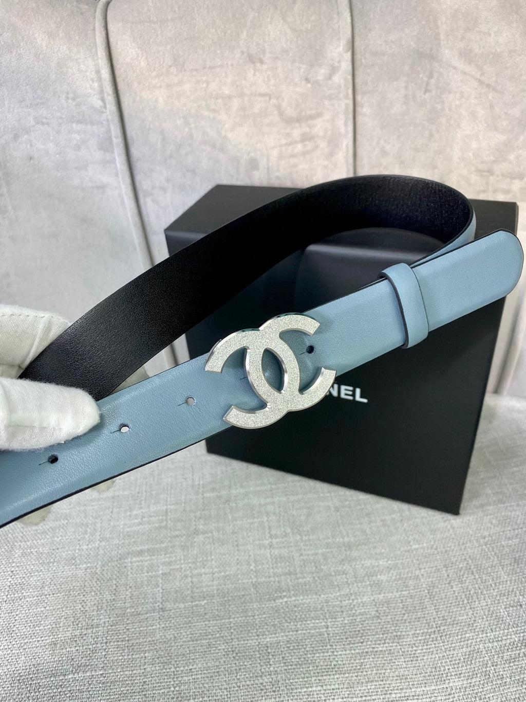 Chanel belt with light blue leather strap and metallic logo buckle, angled view.