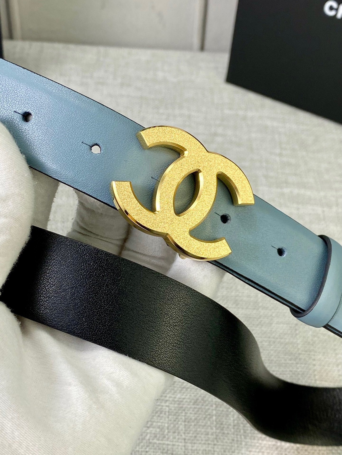 Chanel belt close-up: light blue leather strap with gold logo buckle and pin holes.