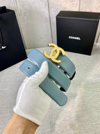 Chanel belt in light blue leather with gold logo buckle, held up for close view.
