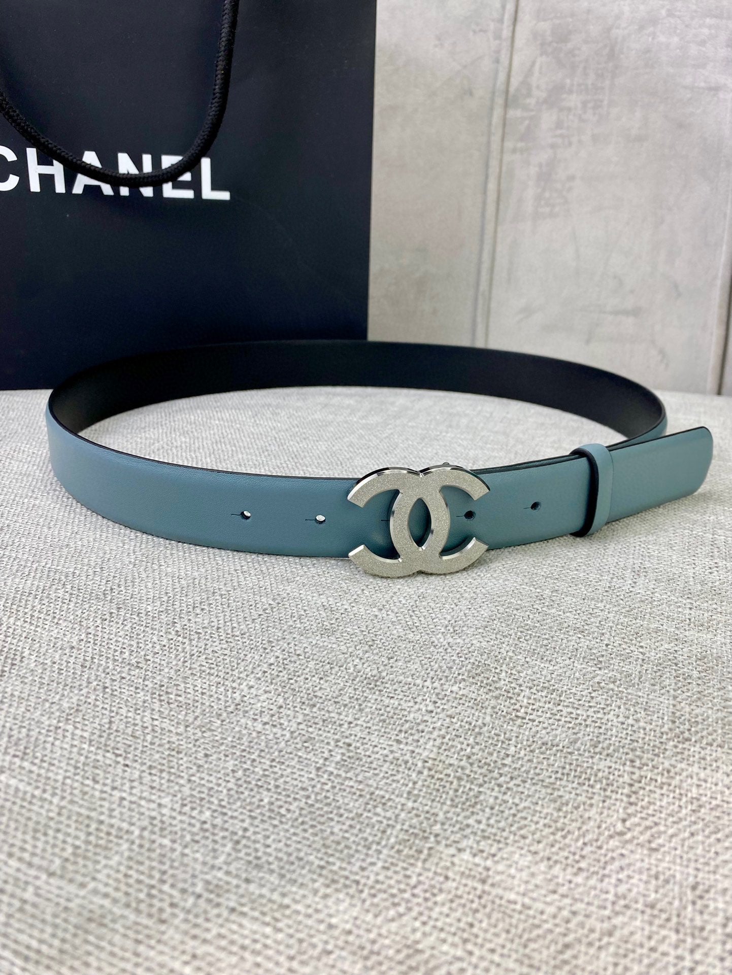 Chanel belt in light blue leather with metallic logo buckle on a curved strap.