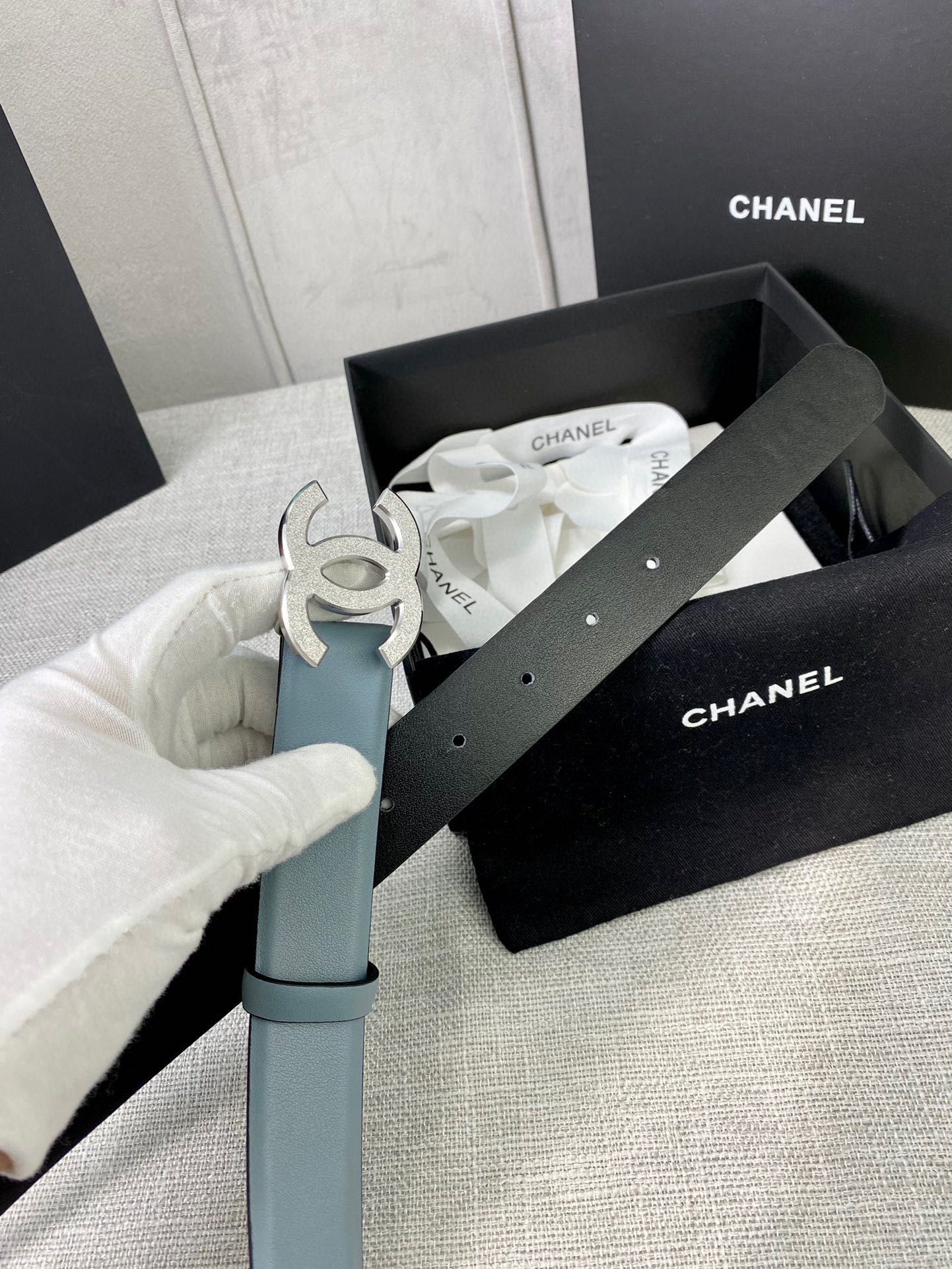 Chanel belt packaging with light blue leather belt and metallic logo buckle visible.