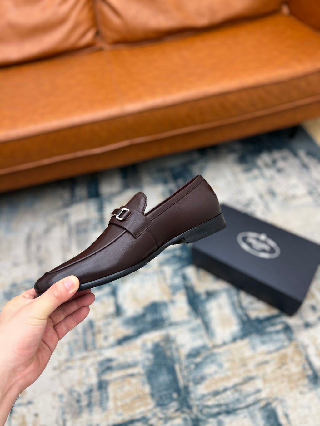 Prada unisex leather loafer with metal buckle strap, dark brown, held up on carpet