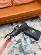 Prada unisex leather loafer with metal buckle strap, dark brown, held up on carpet