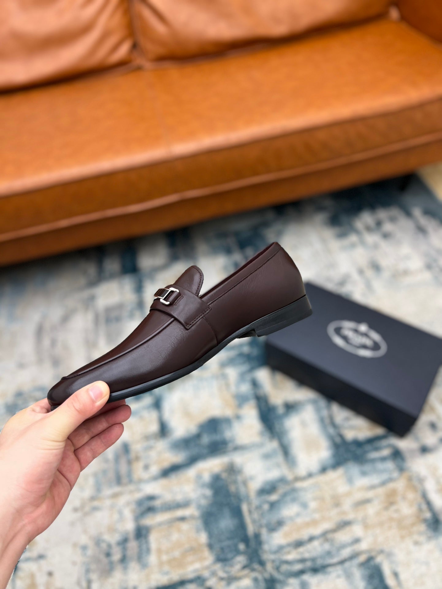 Prada unisex leather loafer with metal buckle strap, dark brown, held up on carpet