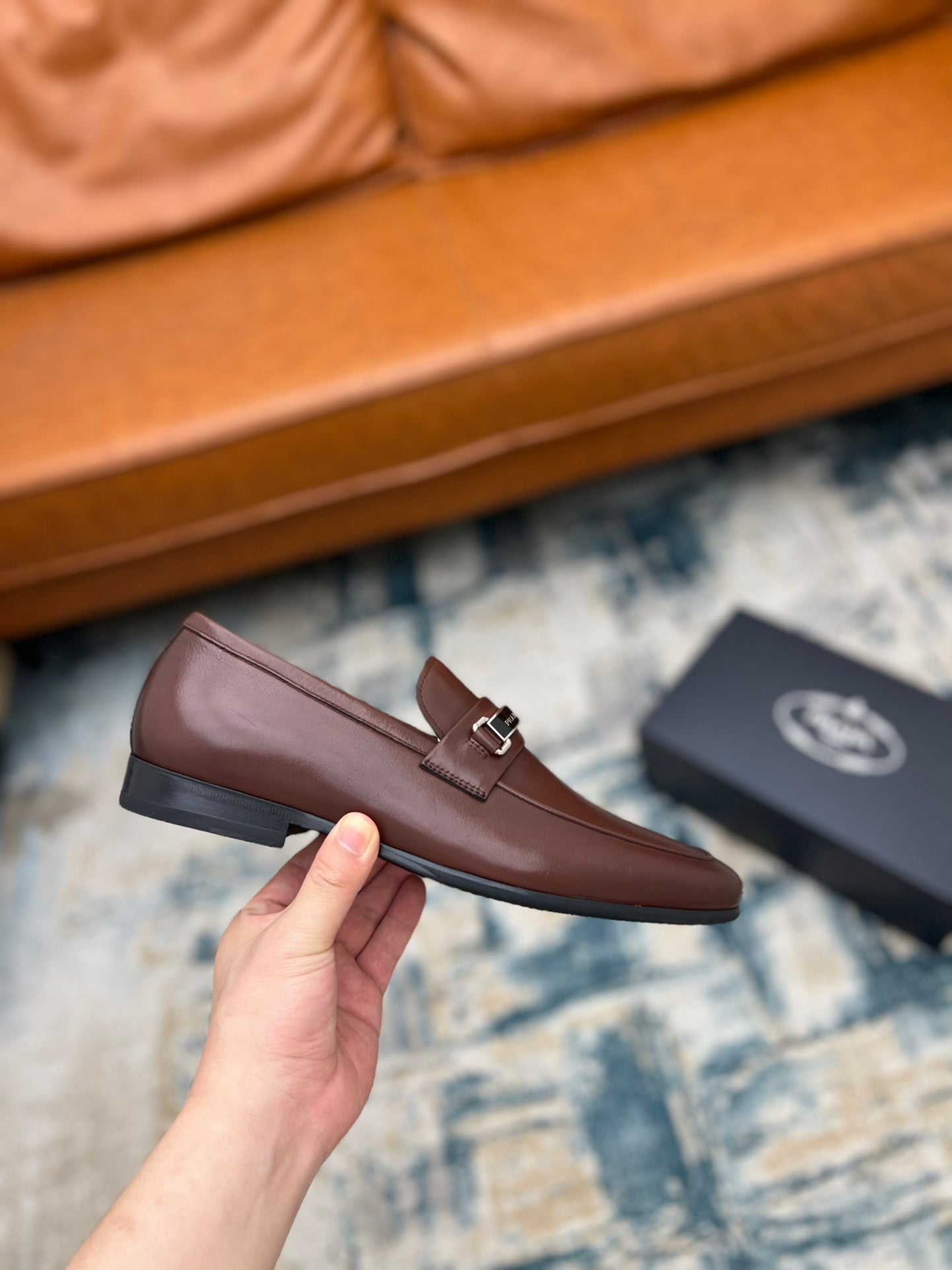 Brown leather loafer with silver buckle strap, held in hand, low profile heel
