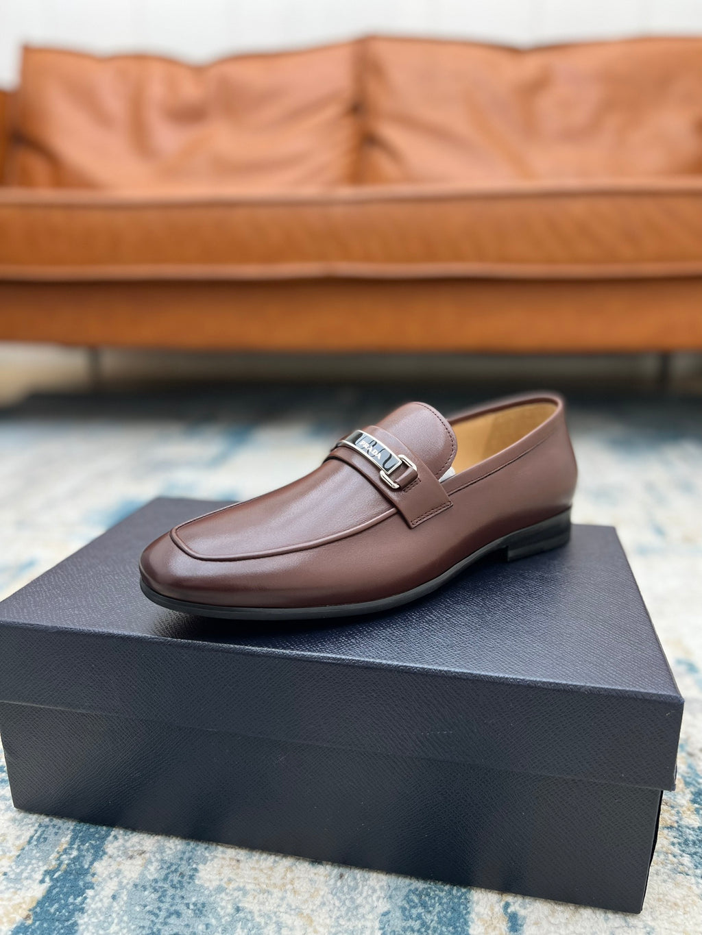 Tan-brown leather loafer with silver buckle strap, low heel, on presentation box