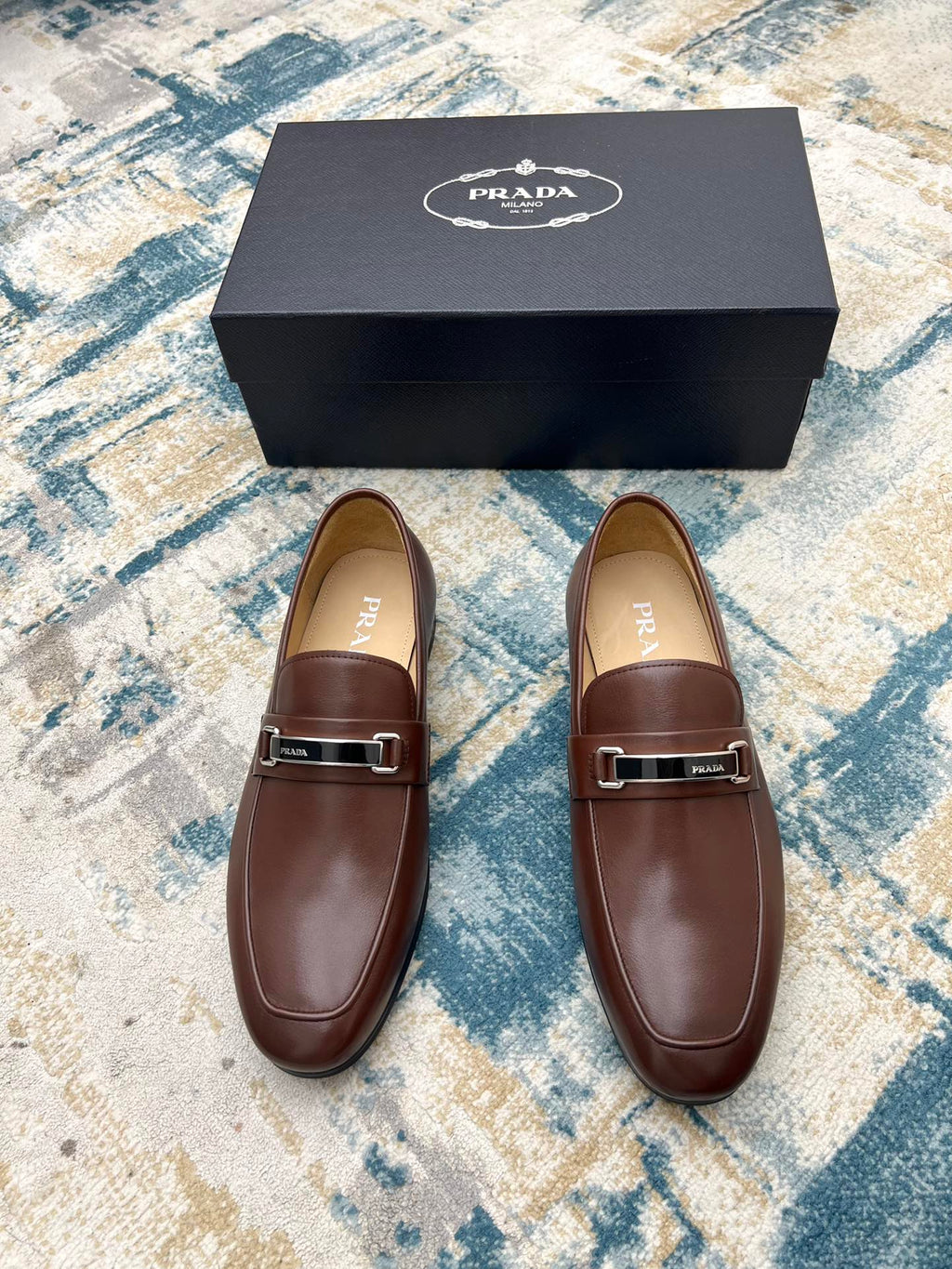 Pair of brown Prada leather loafers with silver buckle strap, shown with gift box