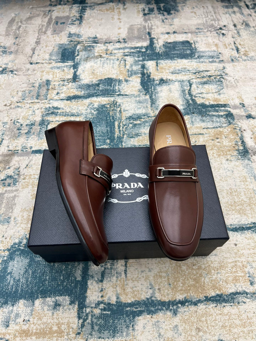 Prada unisex leather loafers, brown with silver buckle strap, side-by-side view