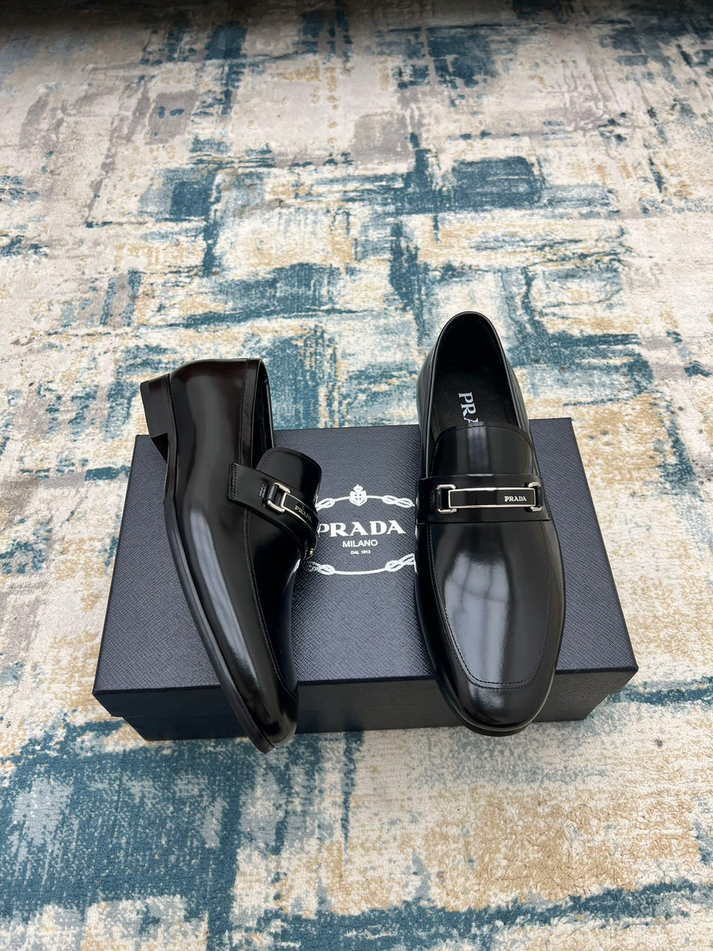 Prada unisex polished black loafers with buckle strap, angled front pair