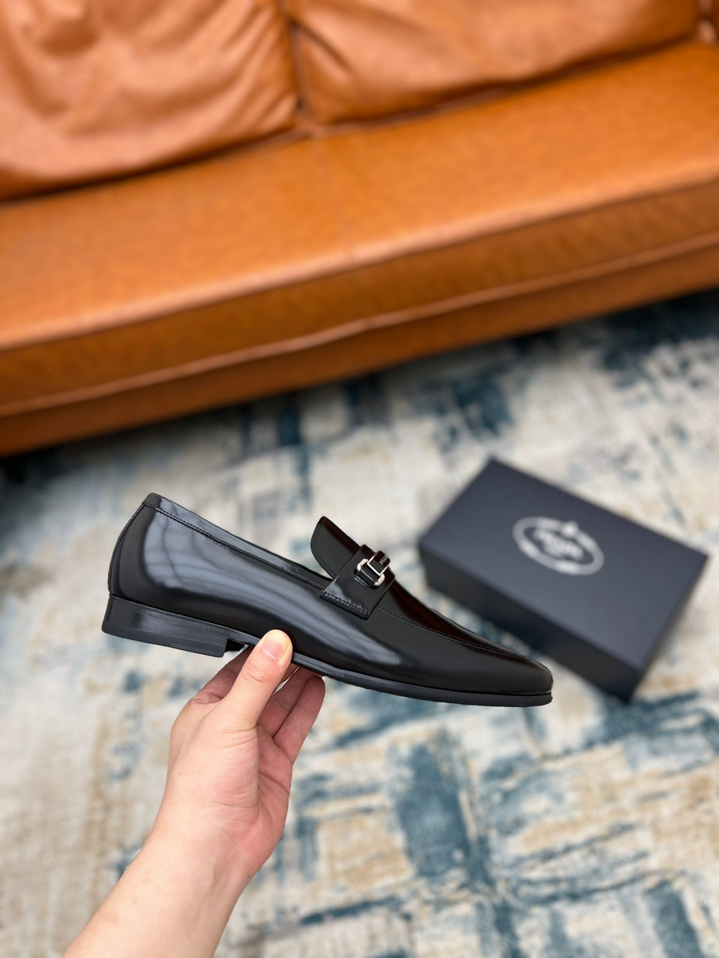 Prada unisex black loafer with buckle strap, held in hand side view