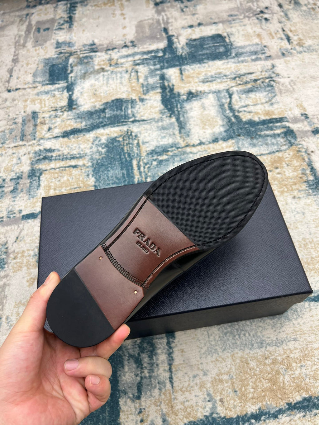 Prada unisex loafers, black outsole and brown footbed, angled view on box.