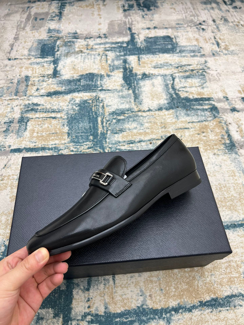 Black Prada loafers with silver buckle strap, rounded toe, side view.