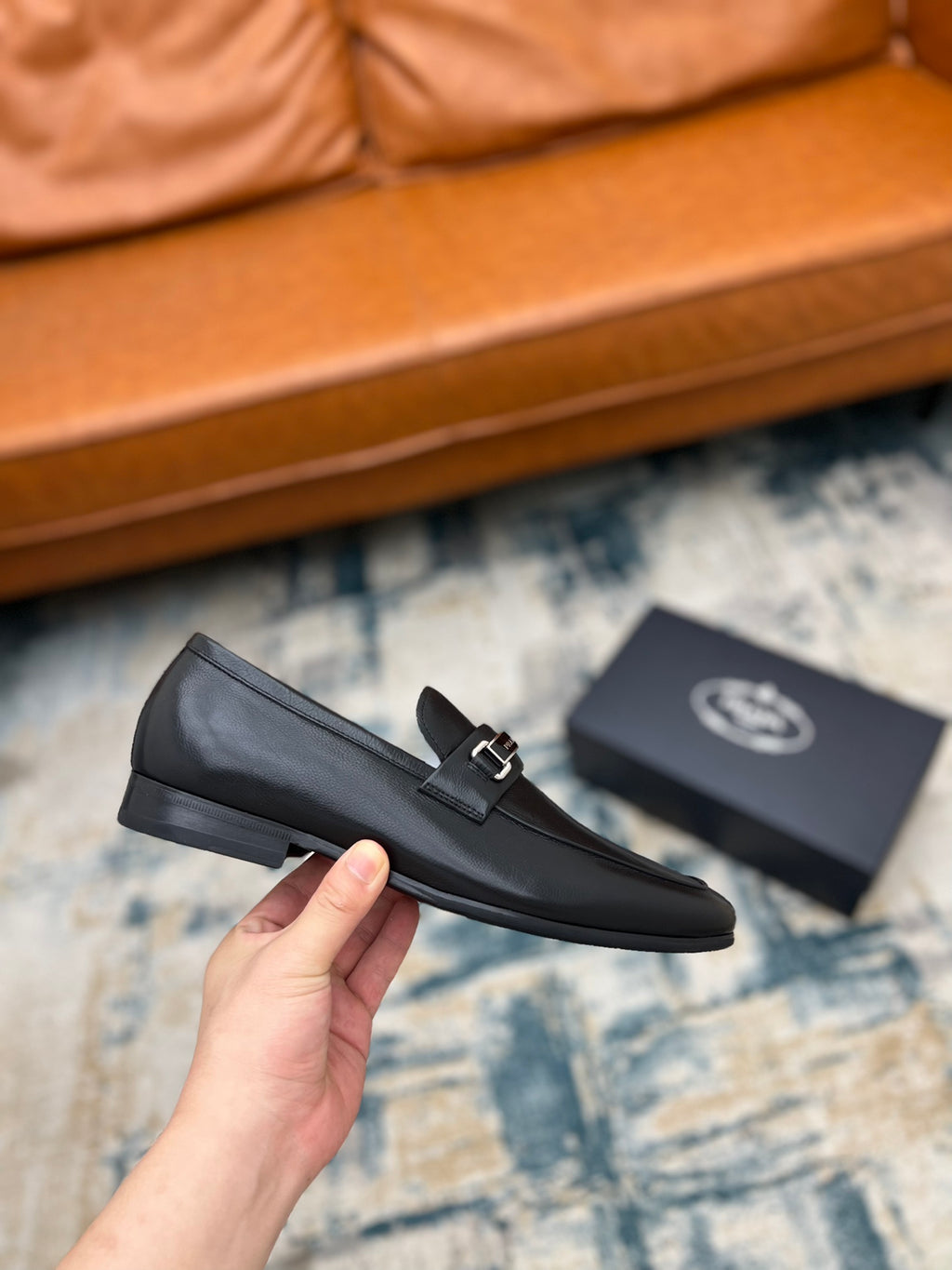 Prada unisex loafers, black leather with silver buckle strap, held in hand.