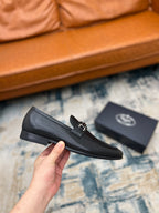 Prada unisex loafers, black leather with silver buckle strap, held in hand.