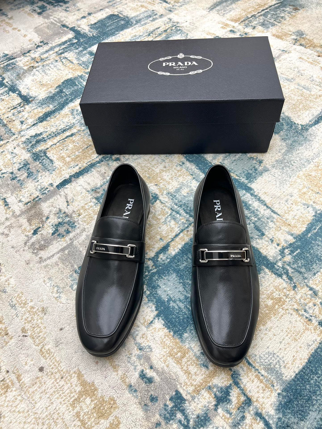 Prada unisex leather loafers, black with silver buckle strap, front view of pair.