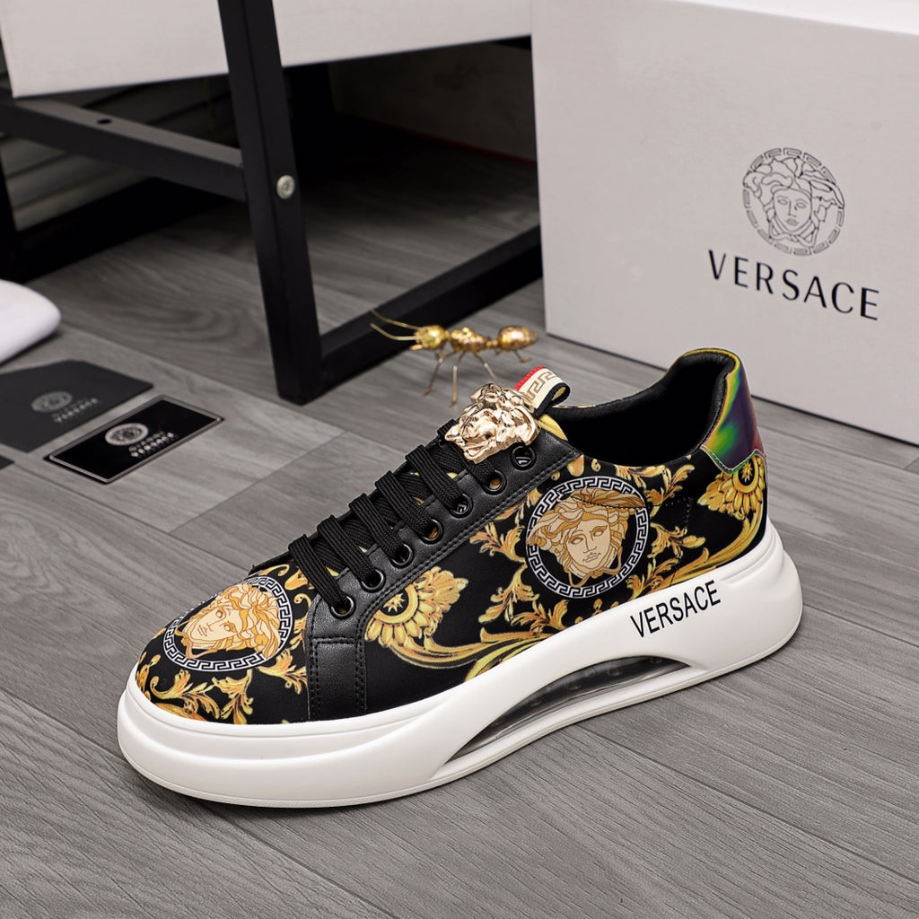 Black low-top sneakers with gold baroque motifs, lace-up design, thick white sole.