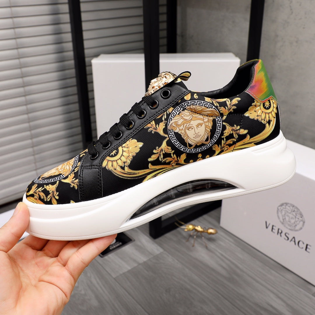 Black low-top sneakers with gold baroque graphics, lace-up front, oversized white sole.