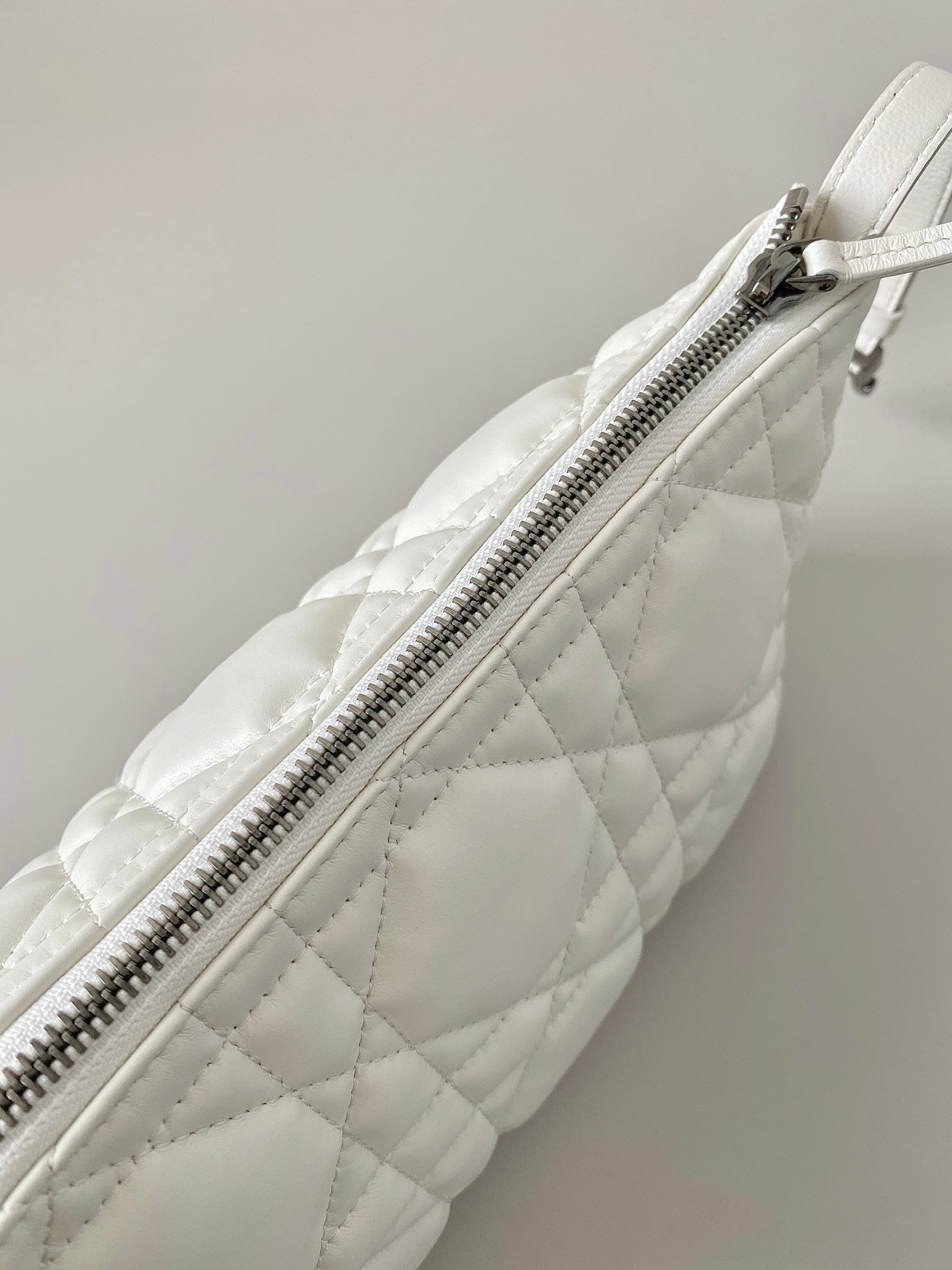 White quilted bag side view with long silver-tone zipper and stitching.