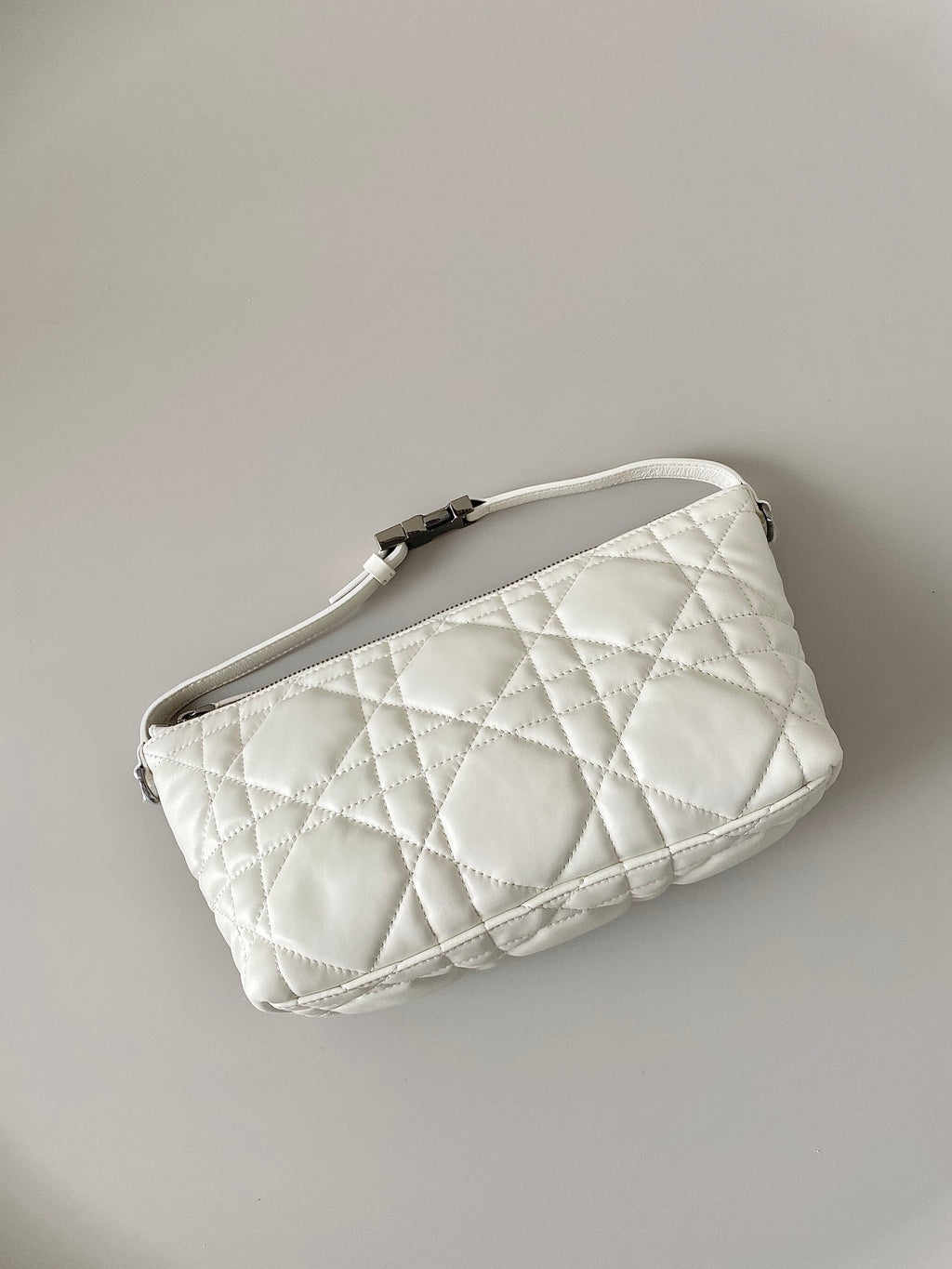 White quilted wristlet bag with top zip and adjustable strap hardware.