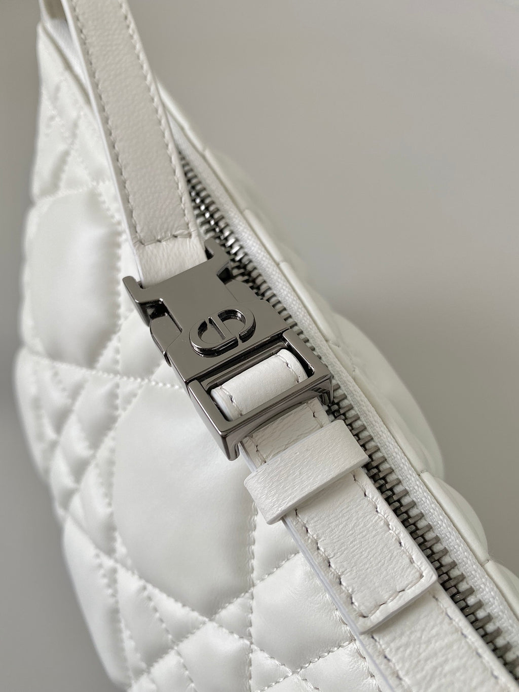 Top zip detail on white quilted Dior bag with metal zipper pull
