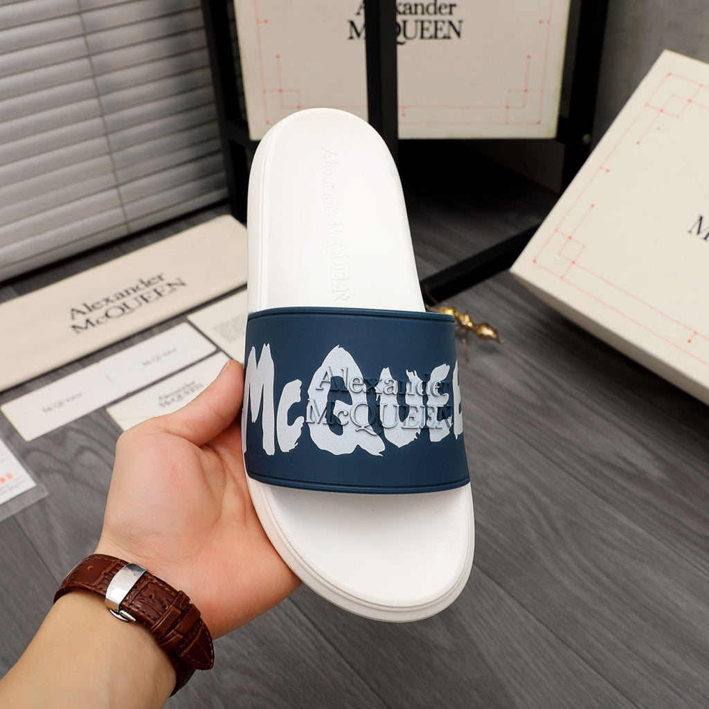 White slide sandal with navy strap and white logo graphic, held in hand