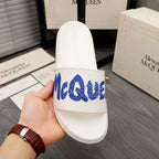 Alexander McQueen white slide sandal with blue logo strap, held in hand